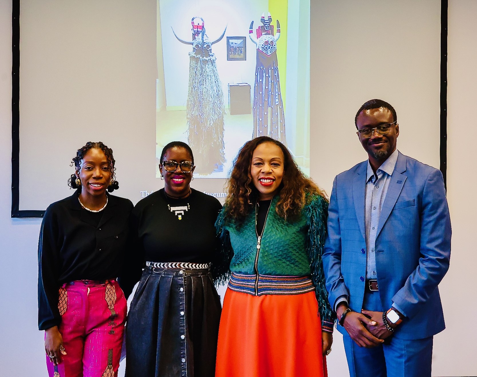 Four colleagues stand in front of a projected image of an artwork smiling at the camera.