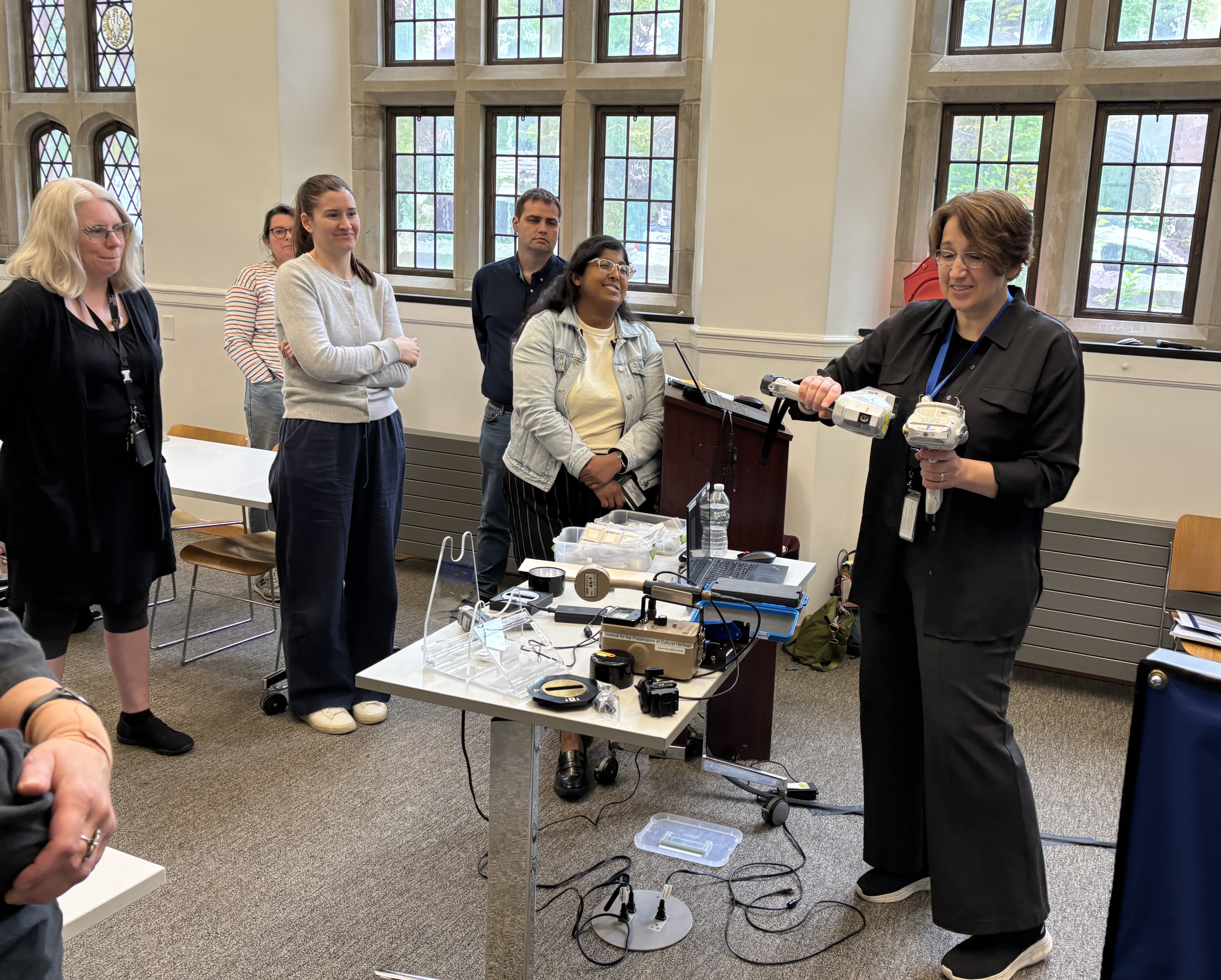 Dr. Aniko Bezur holds two handheld XRF instruments in front of a classroom. 