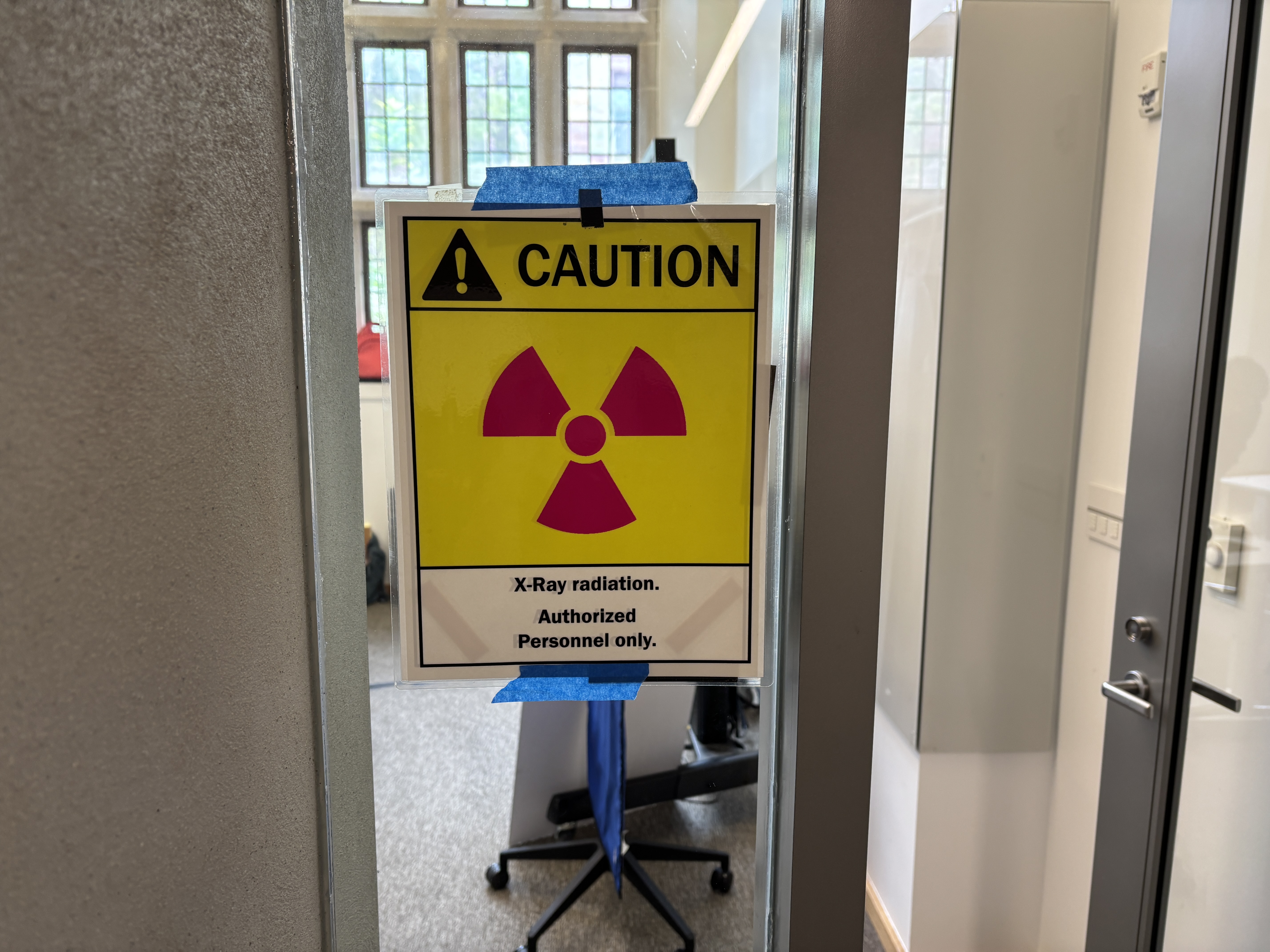 A yellow and red caution sign taped to a classroom window.