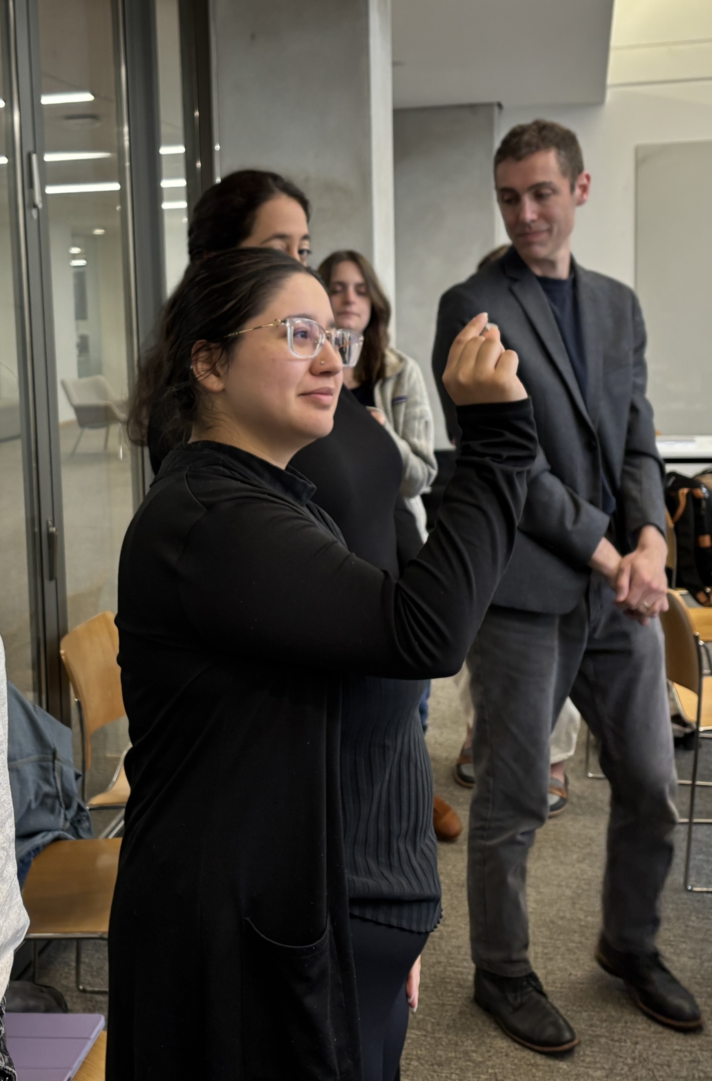 A woman in all black and glasses holds up and examines a small sample.