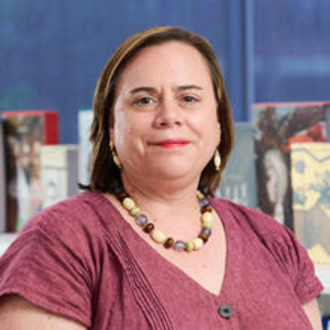 A woman with short brown hair, a beaded necklace and red shirt smiles at the camera.