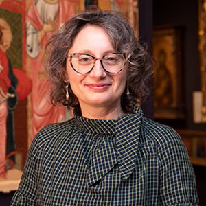 Woman with short wavy hair smiles at the camera wearing glasses and a black and white blouse. 