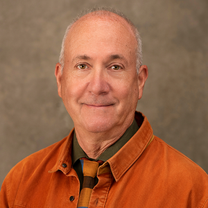 A man with light skin smiles at the camera wearing an orange shirt.