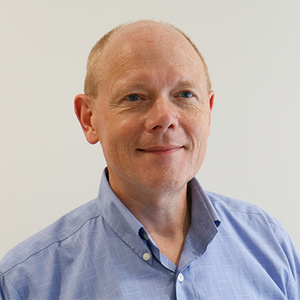 A man with light skin smiles at the camera in a light blue shirt.