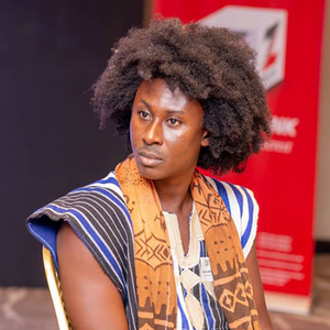 A man with dark skin and an afro looks intensely with colorful patterned clothing.