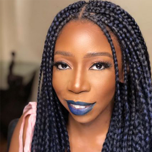 A woman with long dark braids smiles at the camera wearing blue lipstick. 
