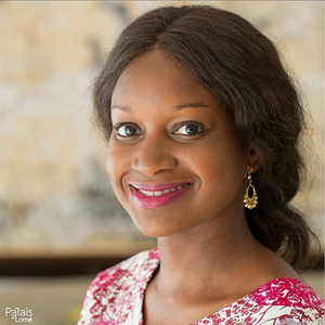 A woman with dark hair and pink lipstick smiles at the camera, wearing gold earrings and a pink top.