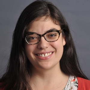 A woman with long dark brown hair and glasses smiles at the camera.