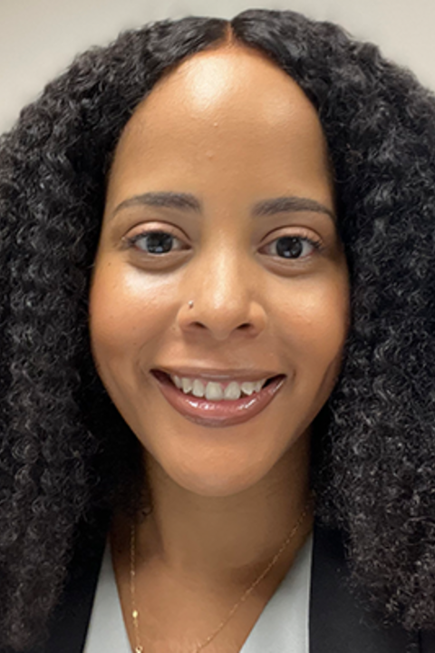 A woman with dark curly hair and a thin gold necklace smiles directly at the camera.