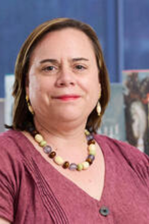 A woman with short brown hair, a beaded necklace and red shirt smiles at the camera.
