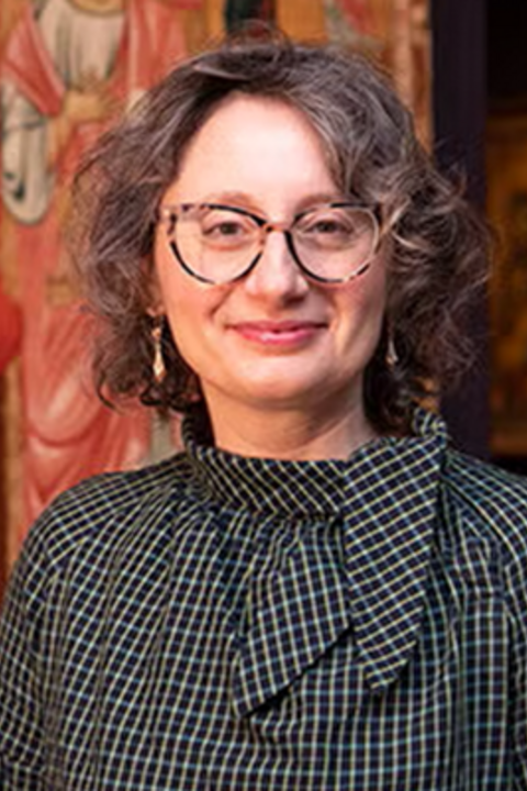 Woman with short wavy hair smiles at the camera wearing glasses and a black and white blouse. 