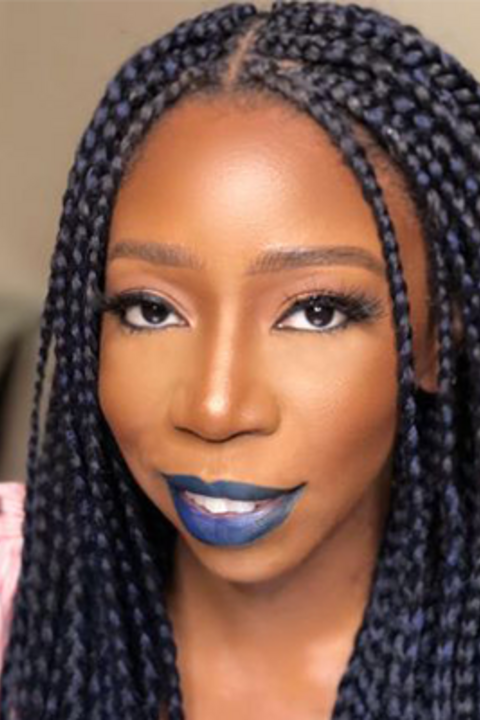 A woman with long dark braids smiles at the camera wearing blue lipstick. 