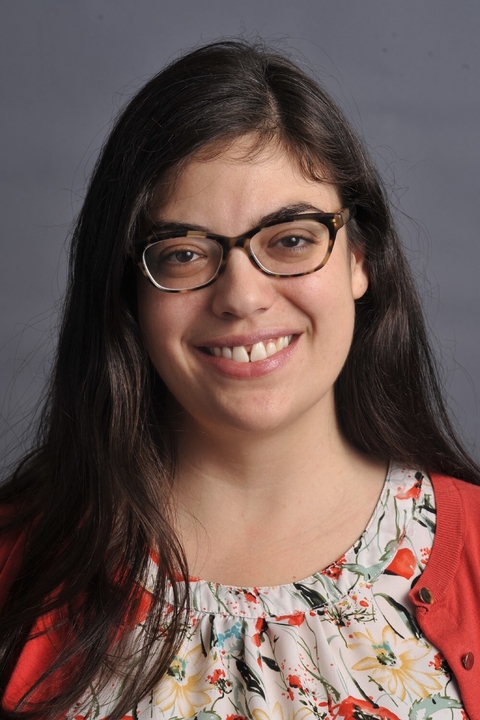 A woman with long dark brown hair and glasses smiles at the camera.