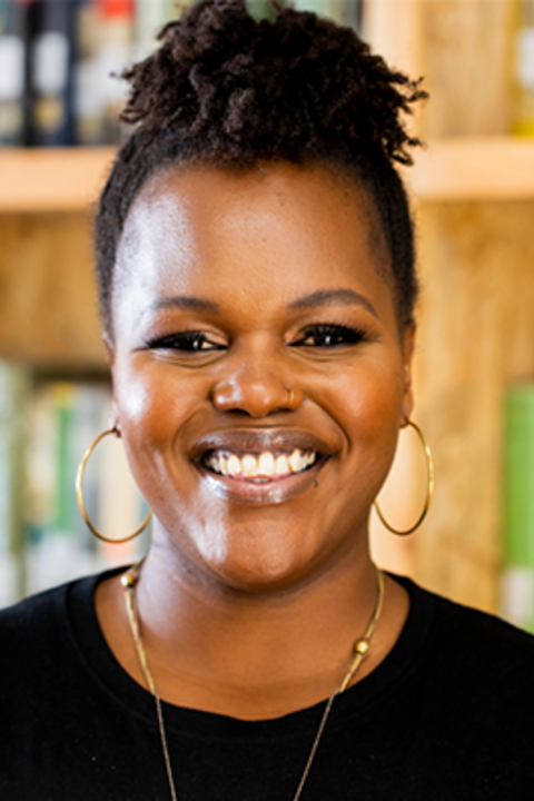 A woman with a black shirt and gold hoop earrings smiles at the camera. 