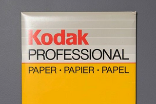 A yellow and gray package of paper with red and black writing on a flat gray background.