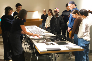 A group of students stand around a table with black and white photos laid out.