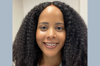 A woman with dark curly hair smiles at the camera.