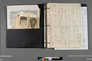 A black binder opened to the front page of aged paper and many papers in the folder pocket.