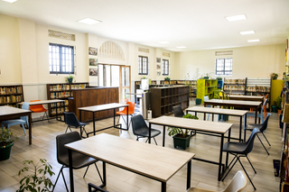 A bright room with tables, chairs, and bookshelves. 
