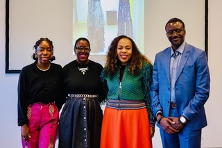 Four colleagues stand in front of a projected image of an artwork smiling at the camera. 