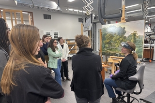 A group of students discuss a landscapt painting with an art conservator. 