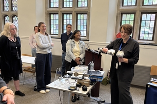 Dr. Aniko Bezur holds two handheld XRF instruments in front of a classroom. 