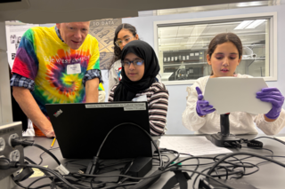 Students hold an art object and begin software on a computer.