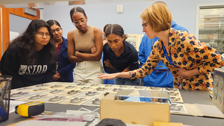 Individuals leaning over a spread of photographs that are varying in paper color. 