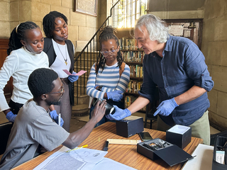 A group of people gather around a table, one holds out an art object with purple gloves.