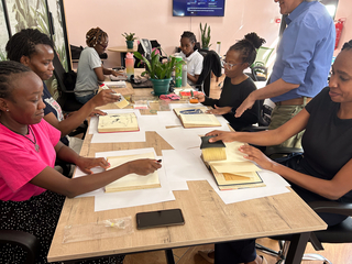 A group of people carefully dust books with large brushes.