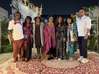 A group of individuals stand on a patterned red carpet. 