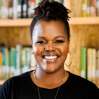 A woman with a black shirt and gold hoop earrings smiles at the camera.