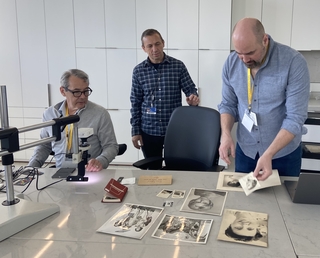 Three colleagues arrange black and white photos in a museum science lab.