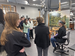 A group of students discuss a landscapt painting with an art conservator.