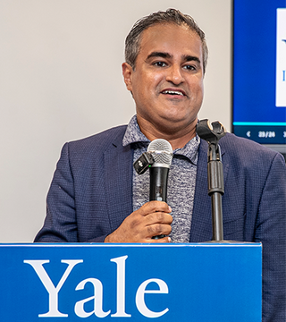 A man holds a microphone behind a podium with the Yale logo.