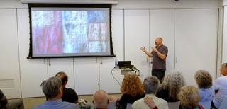 Damon Crockett stands next to a screen showing a colorful artwork while giving a presentation.