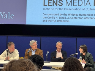 Four speakers sit a table with microphones during a panel discussion.